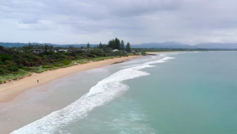 Waves-Splashing-On-Shoreline-With-Tourist-Running-Along-Sandy-Beach-In-Byron-Bay,-Australia
