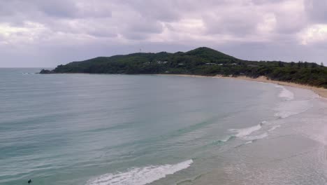 Clear-Blue-Water-Under-Cloudy-Sky-With-Lush-Green-Landscape-Coastal-Town-In-Byron-Bay,-Australia