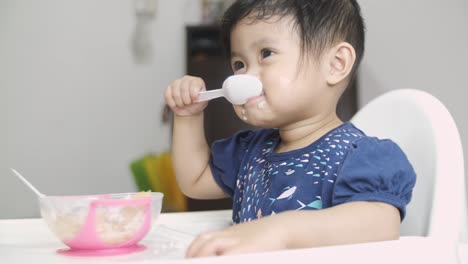 Close-up-shot-of-sweet-little-asian-kid-sitting-on-table-and-eating-fresh-puree