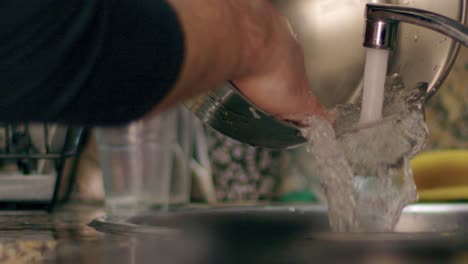 Close-up-of-a-Man-cleaning-a-pan-pot-and-pouring-water-during-house-duties-at-home-in-kitchen-in-super-slow-motion-at-night-medium-shot