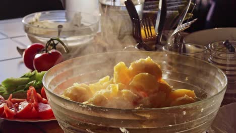Statische-Ansicht-Von-Frisch-Gekochten-Kartoffeln,-Die-In-Einer-Schüssel-In-Einer-Küche-Mit-Frischen-Tomaten-Und-Salat-Im-Hintergrund-Dampfen