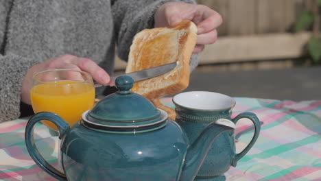 Person-spreads-jam-and-butter-on-slice-of-toast-at-outdoor-English-breakfast