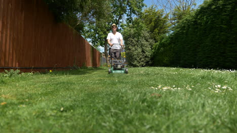 Low,-wide-angle,-slider-shot-of-man-mowing-garden-on-a-sunny-day