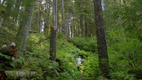 Slow-Motion-Young-Man-Hiking-Downhill-Through-Tall-Trees-in-Wild-Dense-Forest