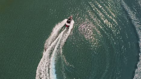 Powerboat-pulls-wakeboarder-across-green-ocean-water,-overhead-circle-aerial