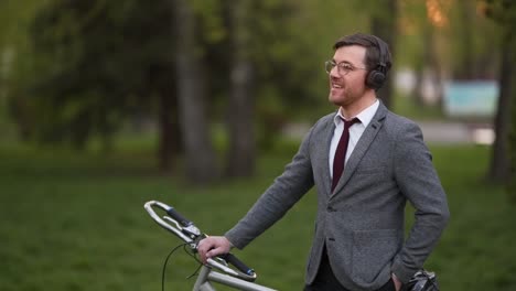 Stilvoller-Junger-Mann-In-Einem-Business-Anzug-Mit-Einem-Fahrrad,-Das-Musik-über-Kopfhörer-Hört