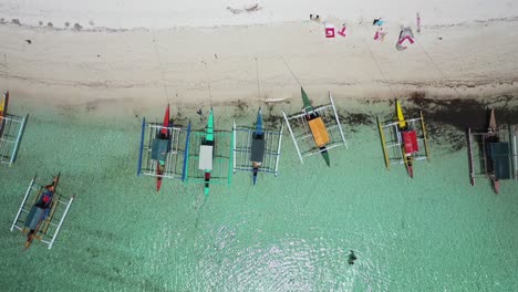 Banca-boats-lined-up-on-Mantigue-Island-white-sand-beach,-overhead-rising-aerial