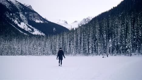 Woman-walks-through-snow-toward-scenic-winter-forest-mountains,-Canada