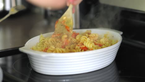Woman-stirring-pasta-with-pasta-sauce-and-tomatoes-in-a-white-bowl