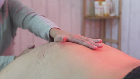 Adult-caucasian-male-getting-a-red-light-infrared-massage-treatment-for-back-pain-from-a-female-physiotherapist,-no-face-closeup-in-slow-motion-with-movement