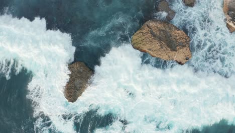 Beautiful-aerial-top-down-view-of-ocean-waves-crashing-into-large-rocks-at-the-shore