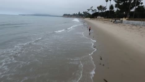 Aerial-of-Woman-Running-Down-Santa-Barbara-Beach-Coastline-in-the-Morning