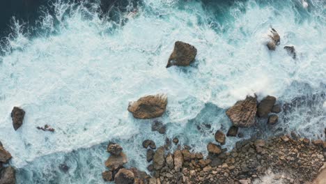Aerial-top-down-view-of-ocean-waves-crashing-into-rocky-shore