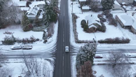 Top-down-aerial-view-of-a-car-traveling-through-a-snow-filled-neighborhood