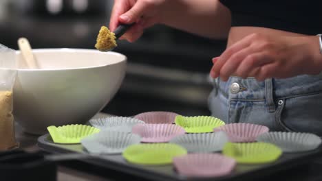 A-woman-is-scooping-and-then-pressing-down-cheesecake-crumb-base-into-a-cupcake-cup