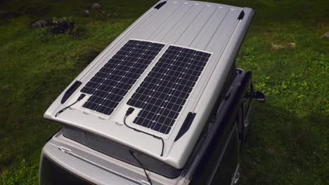 Orbit-drone-shot-of-silver-camper-van-with-two-solar-panels-on-opened-pop-top-roof-tent