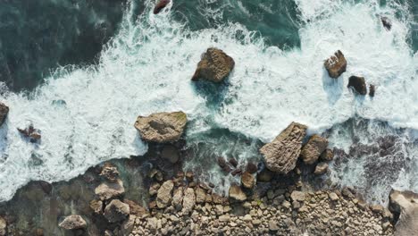 Aerial-top-down-view-of-ocean-waves-crashing-into-golden-rocky-shore