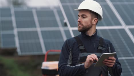 Portrait-of-a-worker-in-a-helmet-with-a-tablet-on-the-background-of-a-solar-power-plant