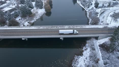 Semi-truck-driving-across-a-bridge-with-snow-covering-the-ground