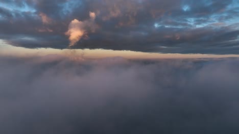Aerial-Reverse-Dolly-Shot-über-Den-Wolken-Während-Des-Sonnenuntergangs-Mit-Warmen-Highlights,-Die-Den-Blauen-Himmel-Und-Die-Grauen-Wolken-Kontrastieren