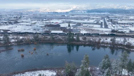 Aerial-view-pushing-over-a-river-and-towards-a-train-with-snow-covering-the-surrounding-ground