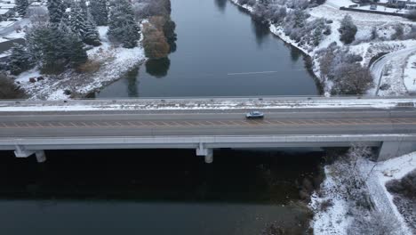Aerial-view-of-a-car-driving-across-a-bridge-with-snow-covering-the-ground