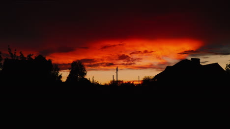 Silhouetted-houses-and-trees-during-fire-red-sunrise,-drone-ascending