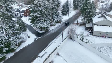 Aerial-view-of-a-dark-car-driving-through-middle-class-America-with-snow-all-around