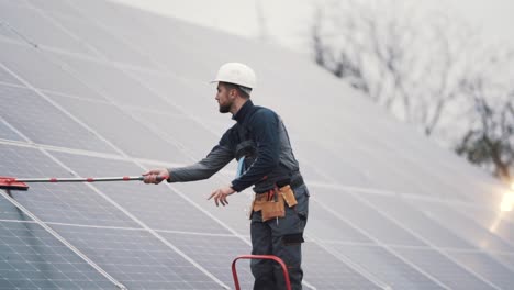 General-shot-of-a-young-man-in-work-uniform-cleaning-solar-panels-with-a-mop