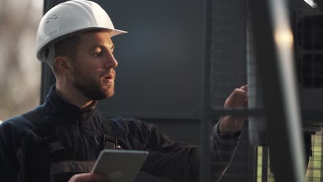 Portrait-of-a-young-male-electrician-at-the-reception-of-the-switchboard-with-a-tablet