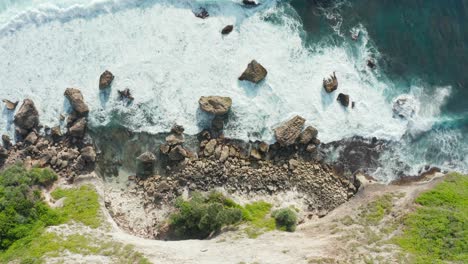 Aerial-top-down-view-of-a-rocky-coastline-with-white-foamy-waves-crashing-into-the-shore