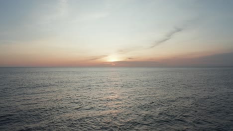 Low-aerial-drone-video-flying-over-water-towards-sun-at-sunset,-sunrise