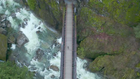 Overhead-aerial-drone-shot-of-a-person-on-suspension-bridge-above-creek-river-going-into-a-cave,-located-in-Othello-Tunnel-Coquihalla-Canyon-Provincial-Park-in-British-Columbia-BC-Canada