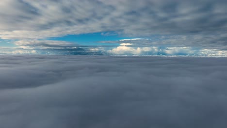 Aerial-view-between-cloud-layers-that-looks-almost-like-sailing-over-the-ocean,-with-blue-sky-and-white-clouds-in-the-distance