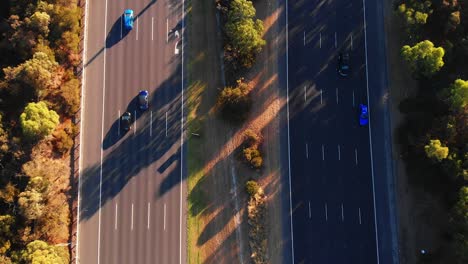 Top-down-birds-eye-view-of-motorway-busy-road-with-green-central-reservation-at-golden-hour-sunset-casting-shadows