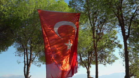 Turkish-National-Flag-Hanging-on-Rope-Between-Trees-on-Sunny-Day,-Slow-Motion
