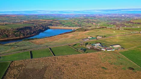 country-road-with-the-M62-motorway-in-the-distance,crossing-Scammonden-Dam-with-farmland-lake,-reservoir,-and-wide-open-views-of-the-Pennine-Hills