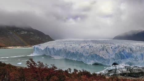 Wide-panoramic-scene-of-Perito-Moreno-glacier-in-Patagonia-in-autumn-season-with-cloudy-sky-and-rainbow-in-background,-Argentina