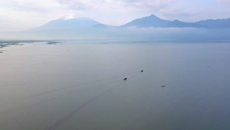 Panorama-drone-shot-of-boats-on-sea-with-gigantic-mountains-behind-clouds-in-background---Asia,Indonesia