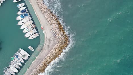Beautiful-aerial-view-of-water-crashing-on-rocks-with-boats-docked