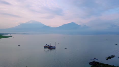 Aerial-view-of-dredger-boat-with-excavator-on-the-huge-lake-with-view-of-mountain-on-the-background---Rawa-Pening-Lake,-Indonesia