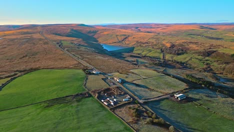 Aerial-drone-footage-of-traffic-on-a-country-road-on-Saddleworth-Moor-with-golden-land-lake,-reservoir,-and-wide-open-views-of-the-Pennine-Hills