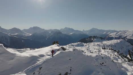 Aerial-shot-in-Switzerland-with-a-person-walking-with-snow-shoes-on-a-sunny-day-with-a-glacier-behind