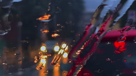 Close-up-of-depressive-bad-weather-with-rain-and-sleet-sliding-down-on-fogged-windscreen-and-blurred-lights-of-car-traffic-in-background