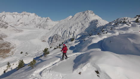 Toma-Aérea-En-Suiza-Con-Una-Persona-Caminando-Con-Raquetas-De-Nieve-En-Un-Día-Soleado-Con-Un-Glaciar-Detrás