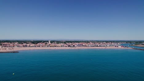 Luftaufnahme-Von-Wunderschönem-Blauem-Wasser,-Einem-Atemberaubenden-Strand-Und-Einer-Kleinen-Stadt