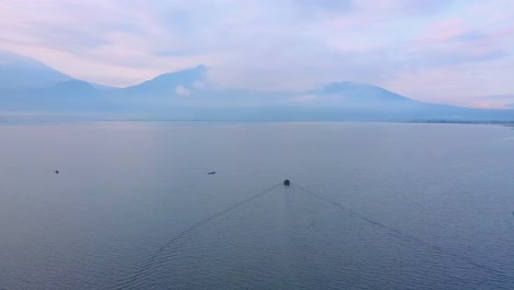 Imágenes-De-Drones-De-Un-Barco-Que-Navega-En-Un-Enorme-Lago-Con-Montañas-En-El-Fondo---Lago-Rawa-Pening,-Indonesia