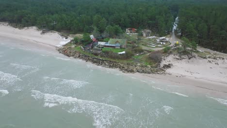 Aerial-establishing-view-of-Baltic-sea-coast-on-a-overcast-winter-day,-distant-house-at-the-beach-with-white-sand,-coastal-erosion,-climate-changes,-wide-drone-shot-moving-forward,-camera-tilt-down