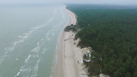 Aerial-establishing-view-of-Baltic-sea-coast-on-a-overcast-winter-day,-a-house-at-the-beach-with-white-sand,-coastal-erosion,-climate-changes,-wide-drone-shot-moving-forward,-camera-tilt-down