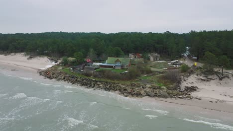 Aerial-establishing-view-of-Baltic-sea-coast-on-a-overcast-winter-day,-a-house-at-the-beach-with-white-sand,-coastal-erosion,-climate-changes,-wide-orbiting-drone-shot